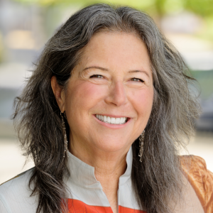 An older white woman with grey-brown hair smiles at the camera.