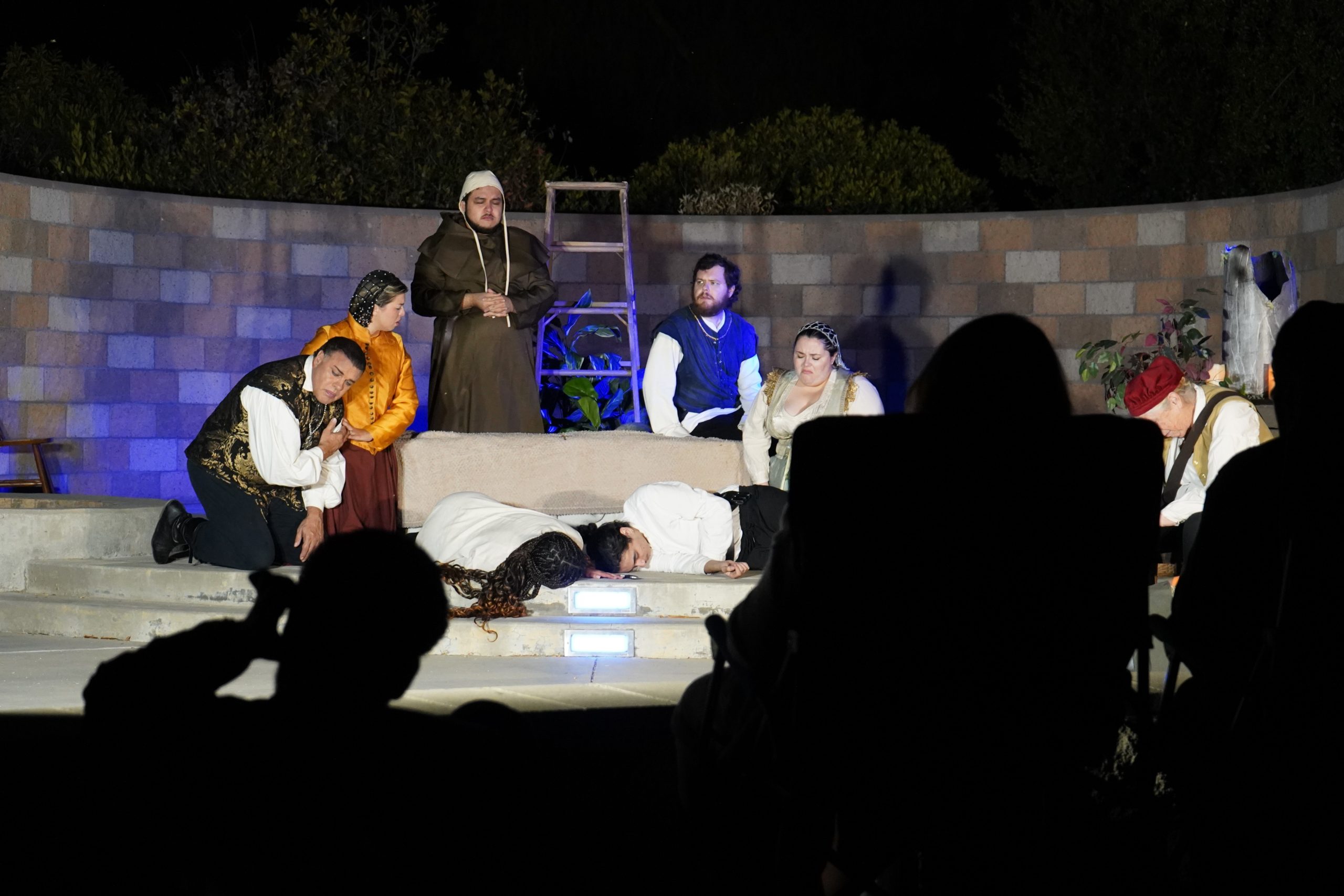 The cast of Romeo and Juliet gather to see the fallen lovers on the ground in front of them.